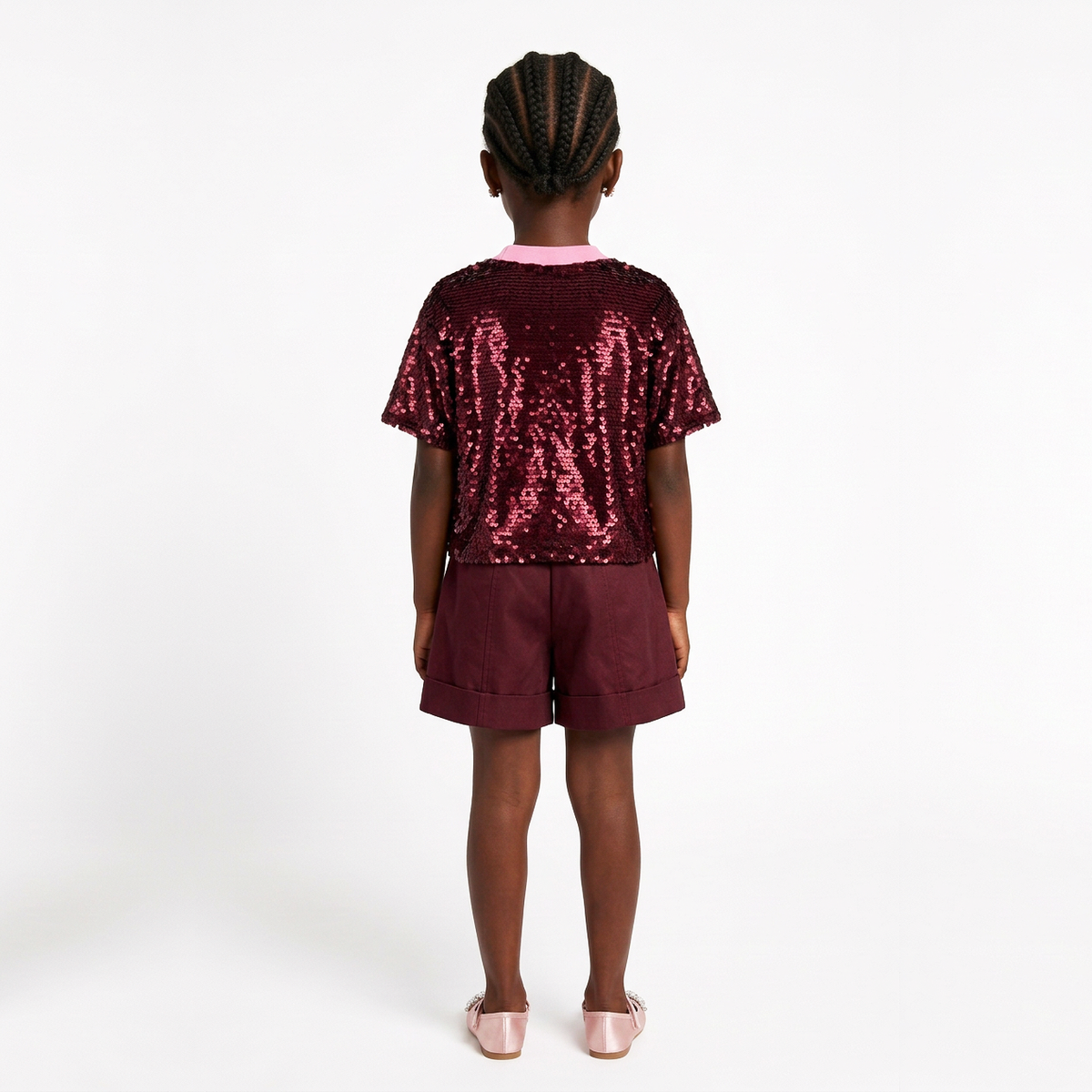 A child model shown from the back wearing a short-sleeve sequined top and matching shorts in a deep burgundy color, paired with light pink shoes, against a plain white studio background.