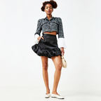 Woman wearing a tweed jacket, black satin skirt, and white shoes on a white background