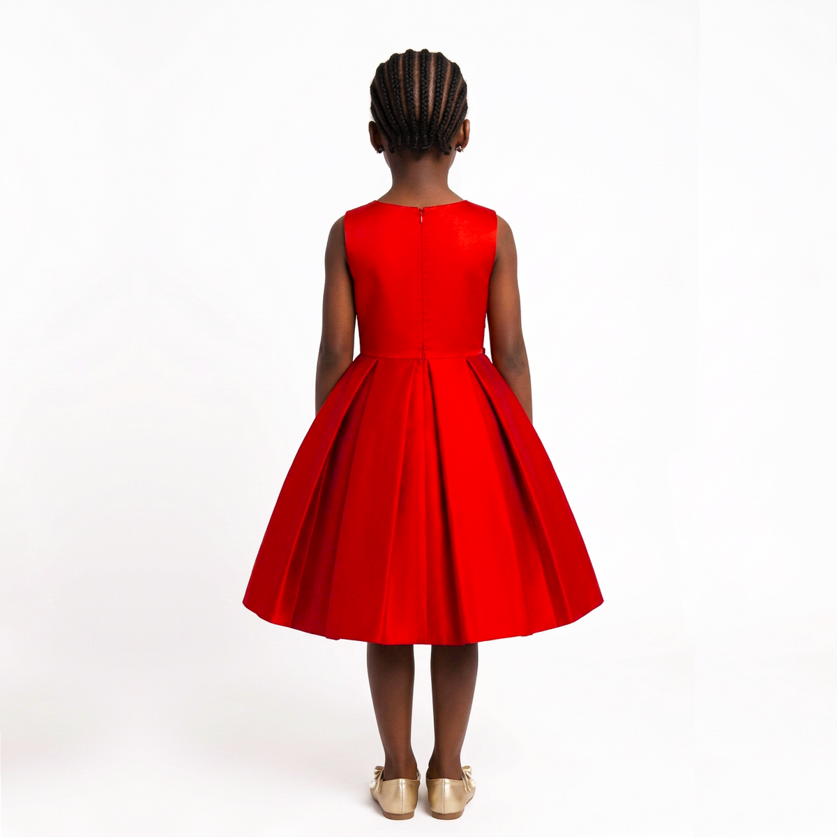 A young girl viewed from behind wearing a bright red sleeveless dress with a pleated skirt and gold shoes, standing against a plain white studio background.