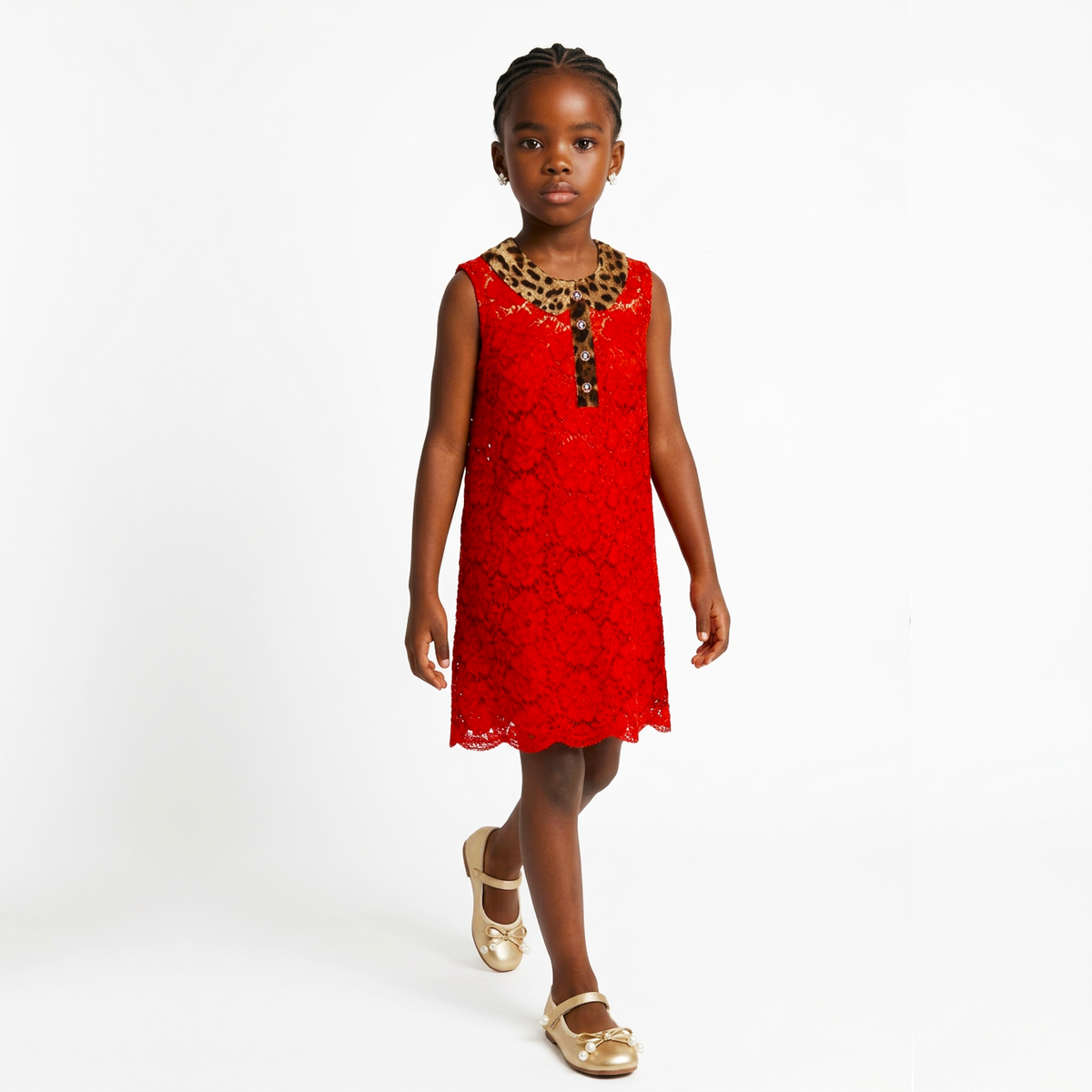 A young girl walking forward in a bright red sleeveless lace dress with a leopard-print collar and gold metallic flats, photographed against a clean white studio background.