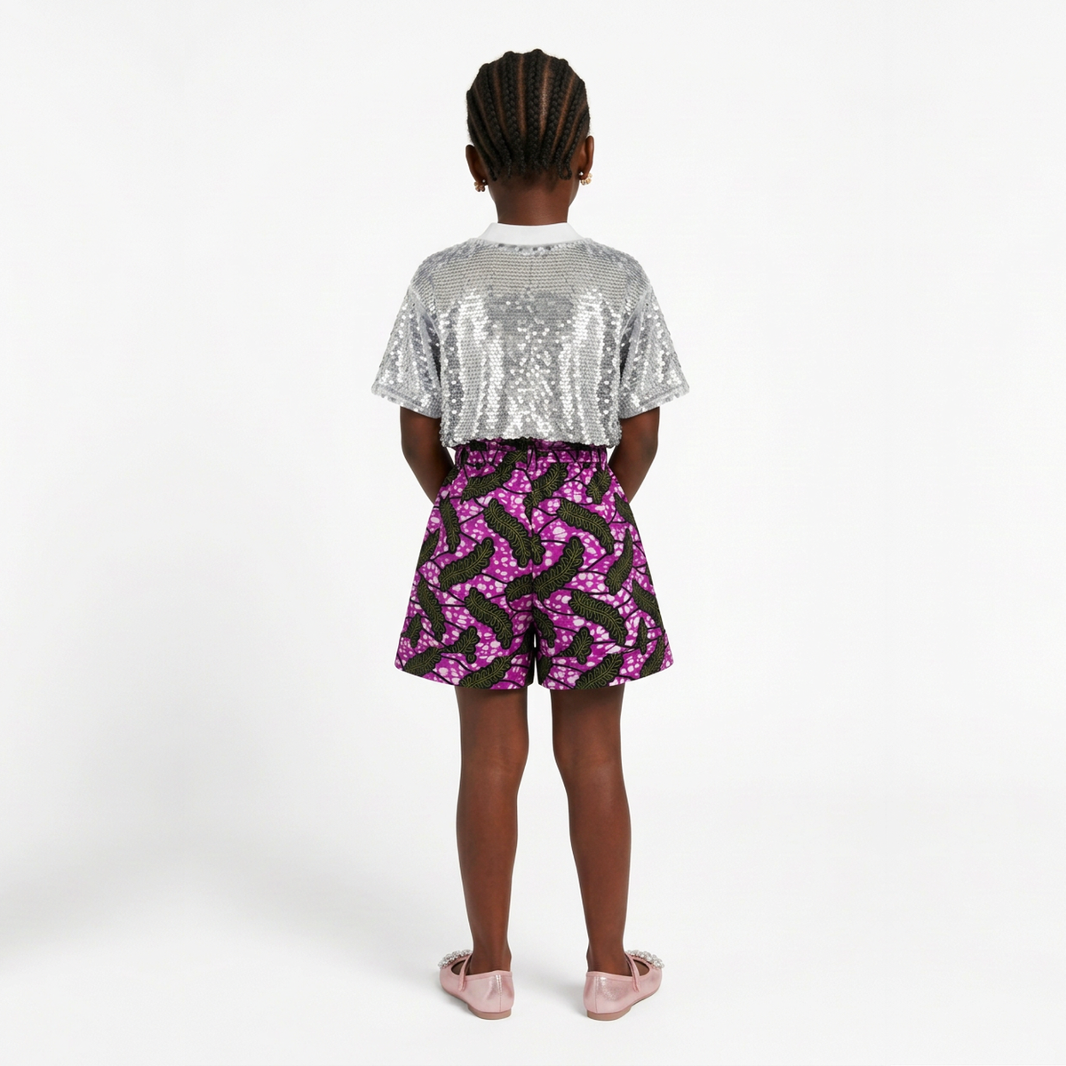 A child model shown from the back wearing a short-sleeve silver sequin crop top and a black skirt with a pink floral pattern, set against a plain white studio background.