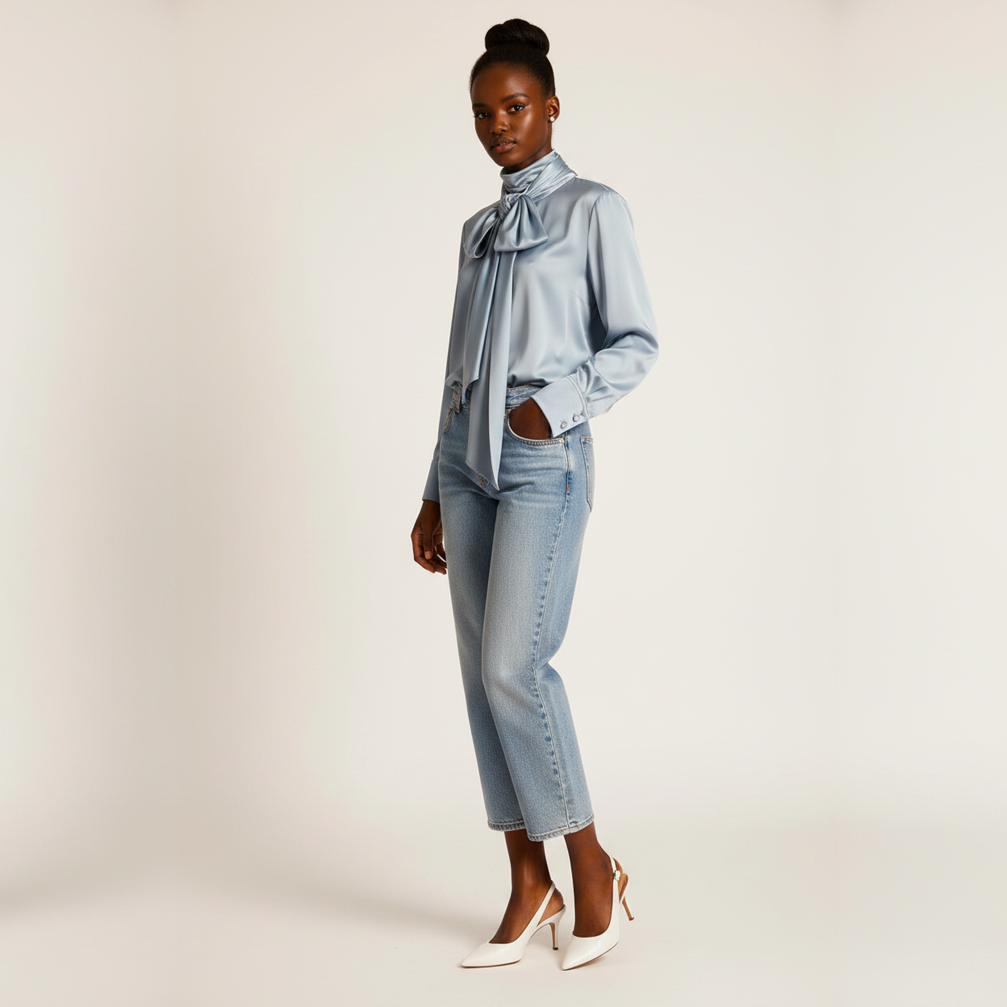 Woman wearing a light blue blouse with a bow tie and jeans on a plain background