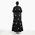 Black dress with white floral patterns worn by a model on a white background
