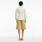 Woman wearing a cream blouse and beige pants on a white background