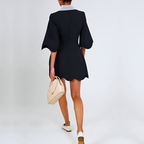 Person wearing a black dress holding a beige handbag on a plain background