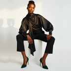 Woman wearing a black outfit with a draped top and green high heels on a white background