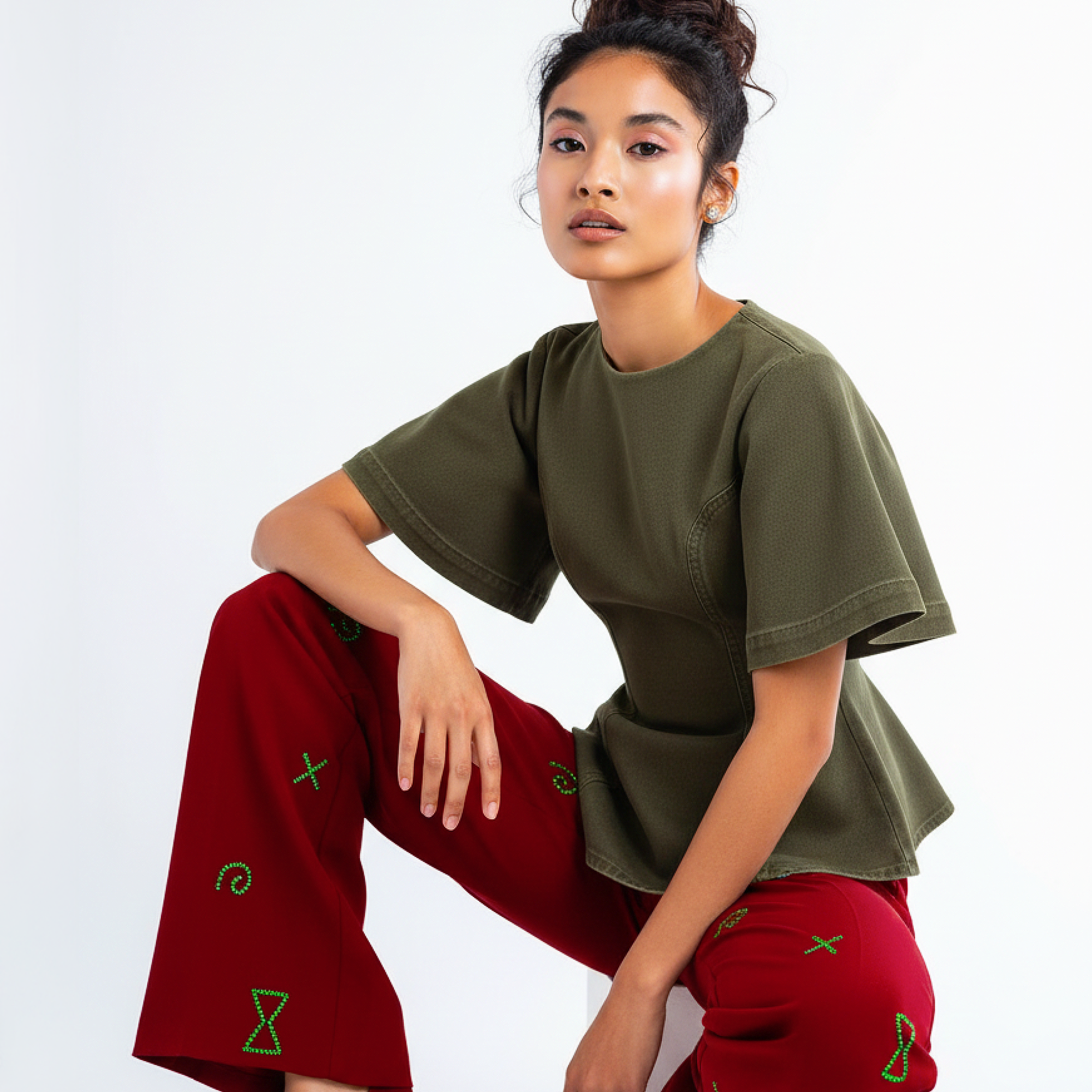 Woman wearing an olive green top and red pants with green patterns on a white background