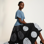 Model wearing a blue top and black skirt with white circular patterns on a plain background