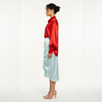 Woman wearing a red satin shirt and light blue skirt on a white background