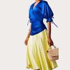 Woman wearing a dress with a  blue top and yellow skirt with a beige handbag on a light gray background