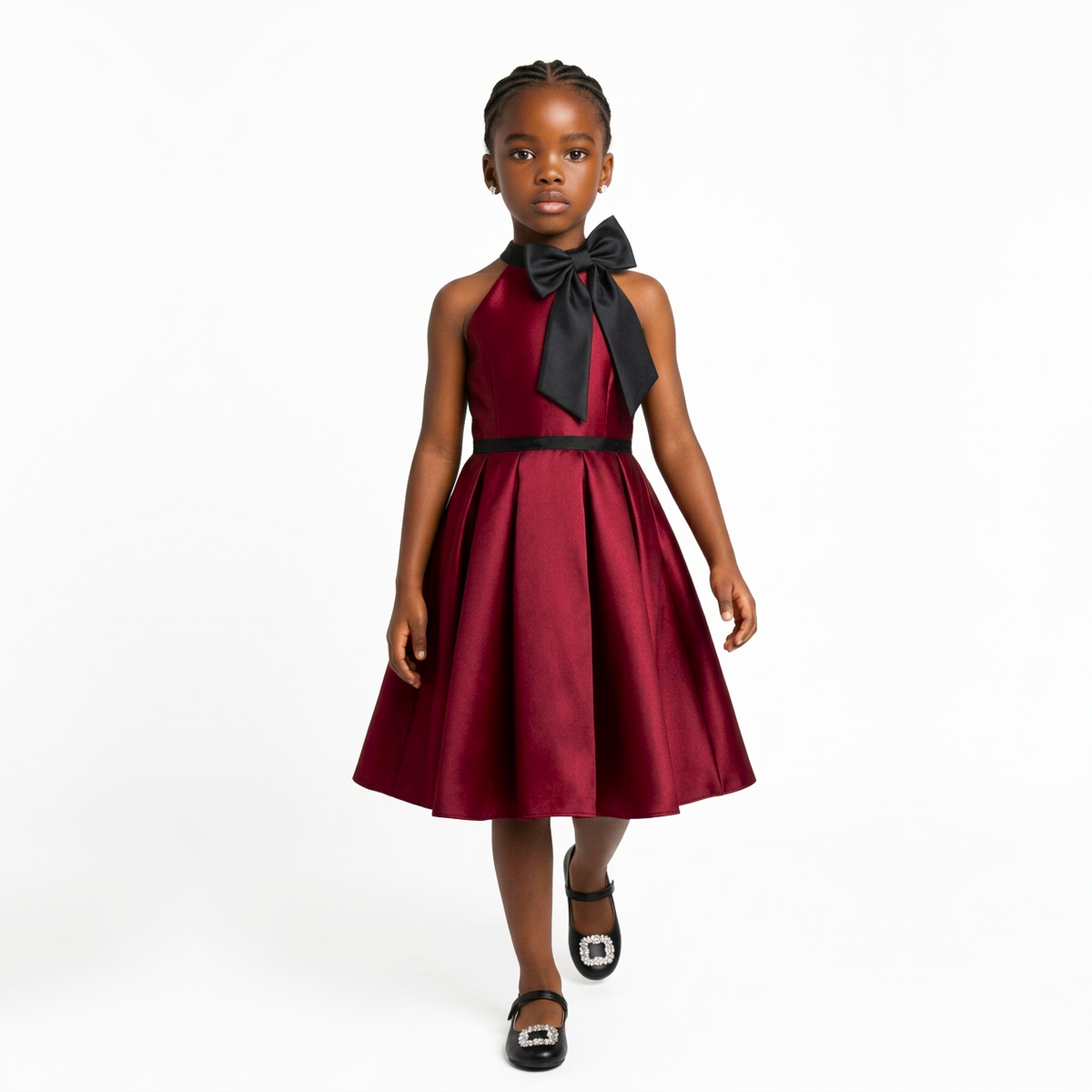A young girl modeling a sleeveless halter-neck dress in deep burgundy with a large black bow at the neckline and a matching black waistband, photographed against a plain white studio background.