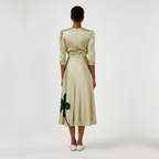 Woman wearing a beige dress with green clover patterns on a white background