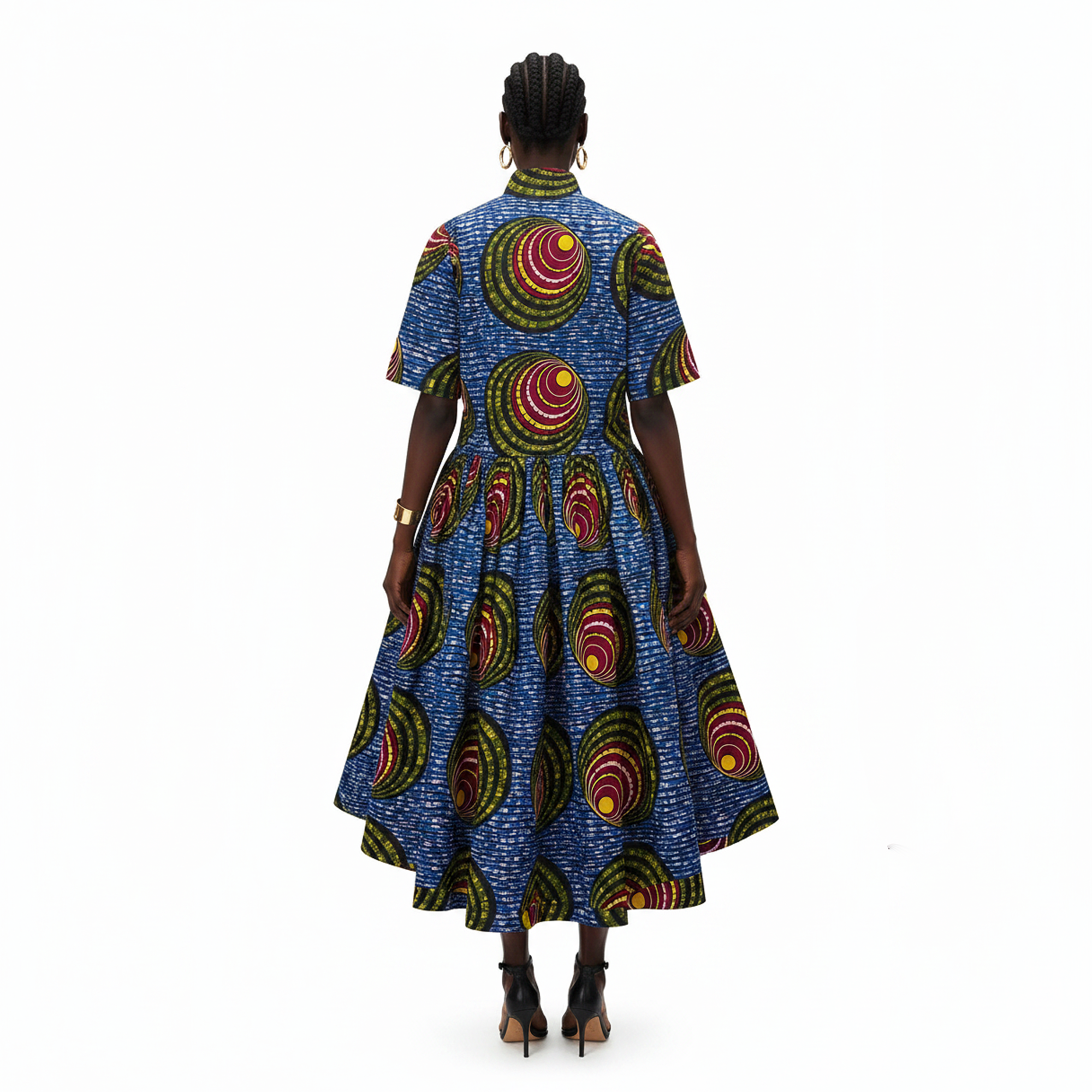 A woman viewed from the back wearing a short-sleeve high-neck midi dress with a vibrant blue base and circular multicolor African wax print, paired with black high-heeled sandals against a plain white background.