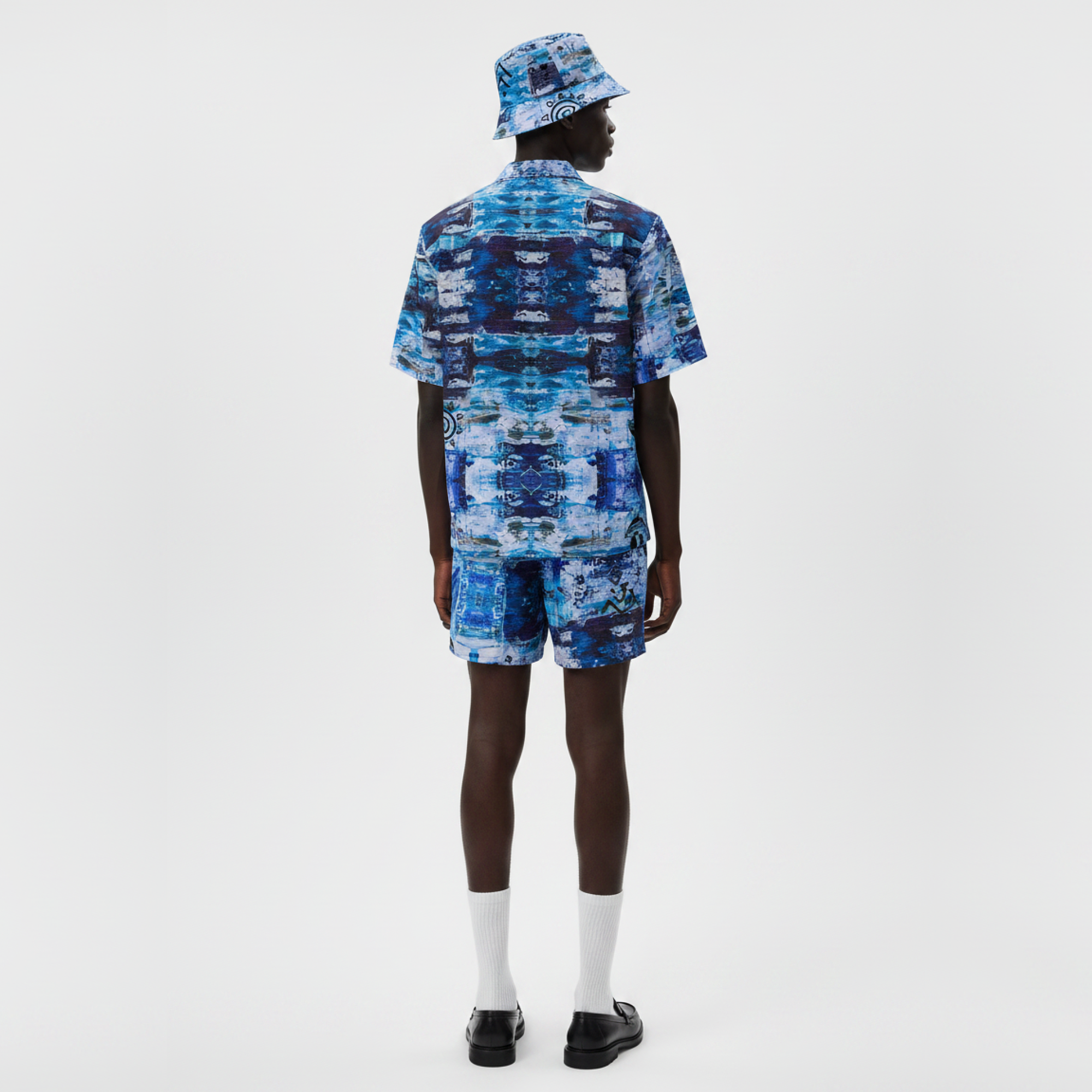 Person wearing a blue patterned outfit with a bucket hat on a white background