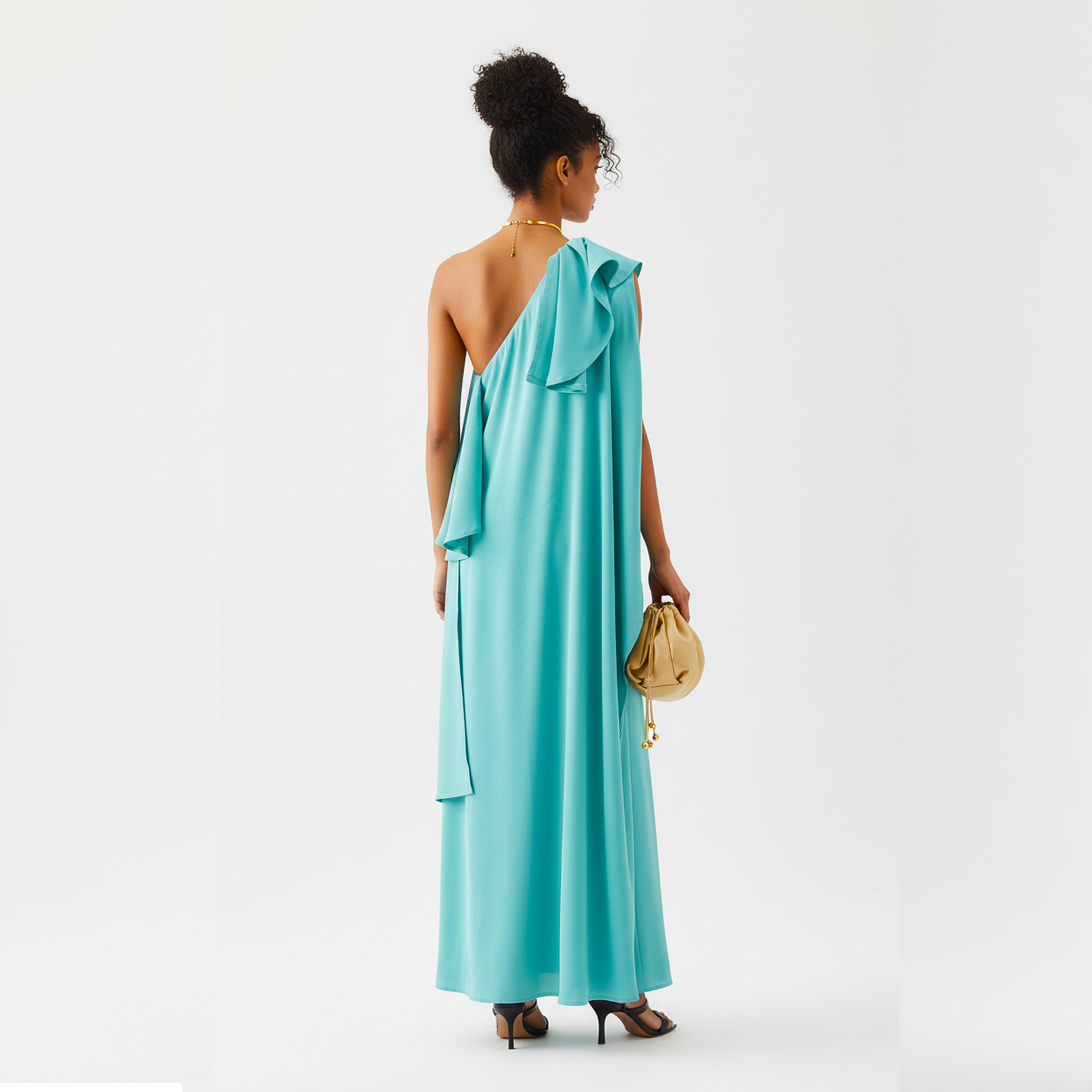 Woman wearing a turquoise one-shoulder dress holding a gold handbag on a white background