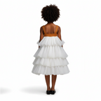 Young girl wearing a white tiered dress with a brown top on a black background