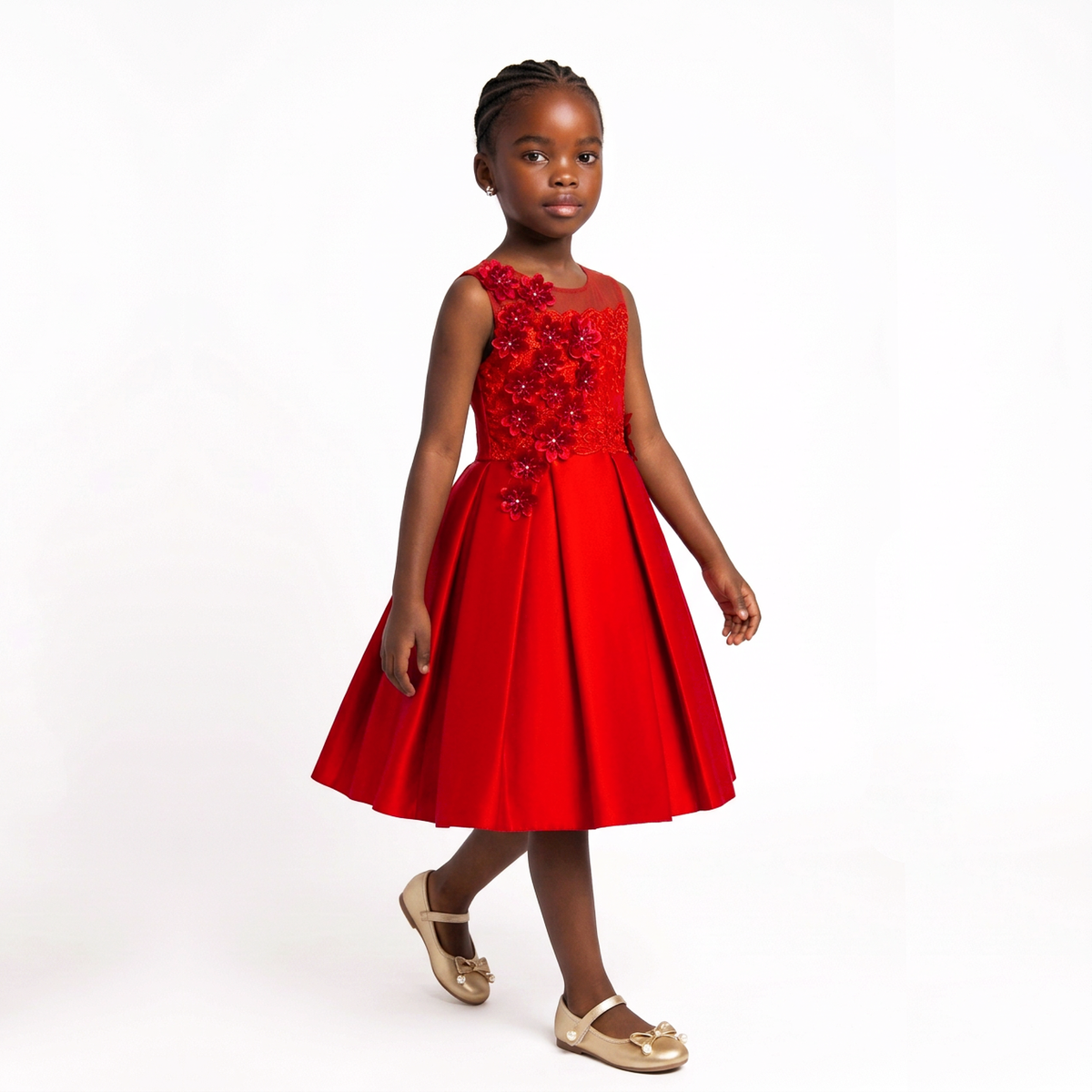 A young girl wearing a bright red sleeveless dress with a beaded floral bodice and a flared skirt, paired with gold flat shoes, standing against a plain white studio background.
