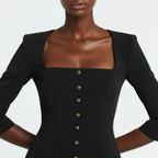 Black dress with gold buttons worn by a model on a white background