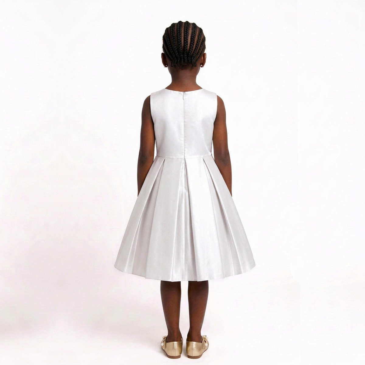 A young girl viewed from behind wearing a sleeveless white dress with a pleated skirt and a straight neckline, standing against a plain white studio background.