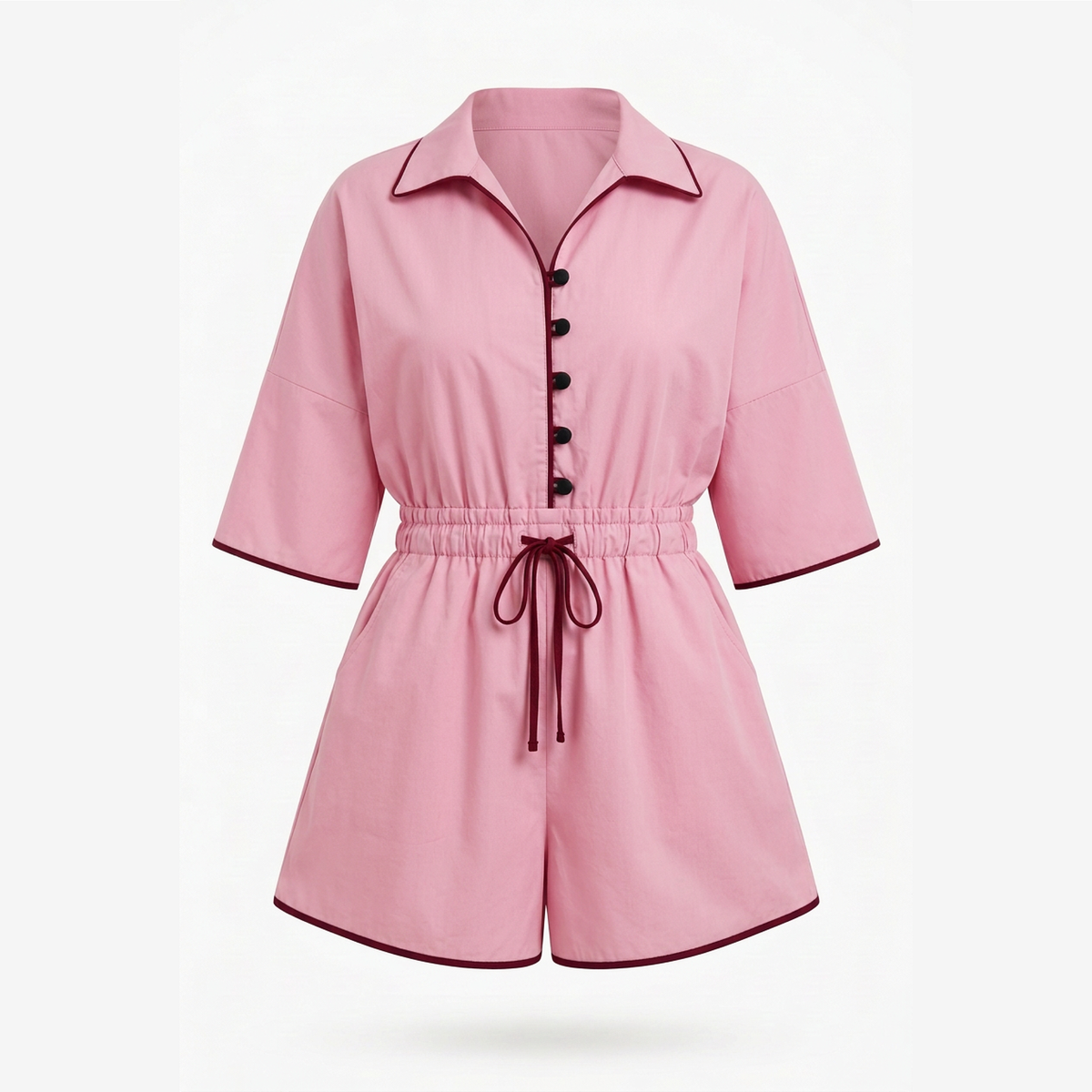 A pink short-sleeve romper with a pointed collar, black front buttons, an elastic waist, and a matching drawstring tie, shown on a light gray background.