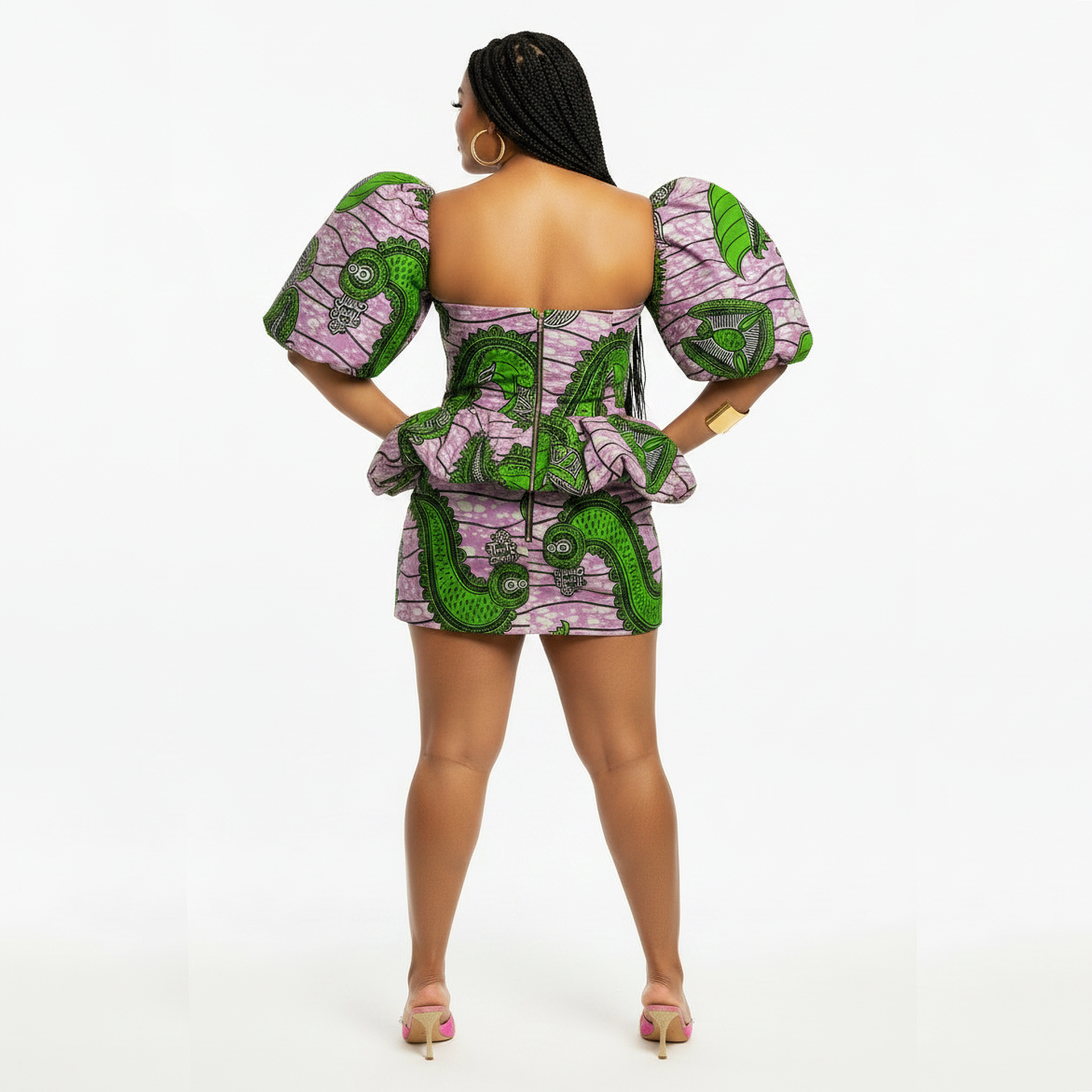 A woman shown from the back wearing a short puff-sleeve dress with a bold green and pink pattern, photographed against a plain white studio background.
