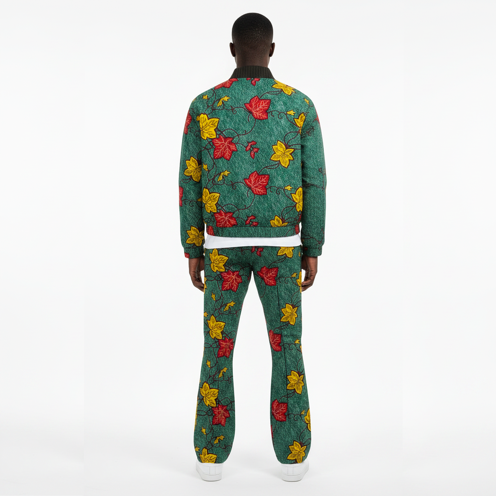 A model shown from the back wearing a matching green tracksuit with a red and yellow leaf pattern, a dark ribbed collar, and white sneakers against a plain white background.