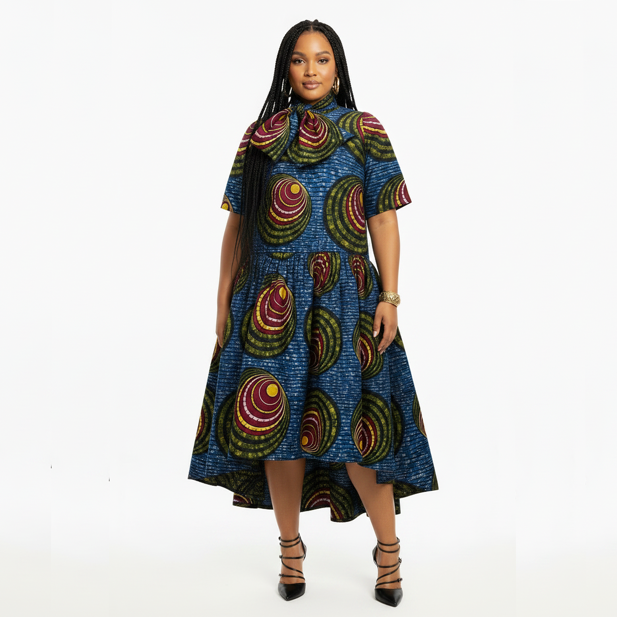 A woman modeling a short-sleeve high-low midi dress with a vibrant blue base and a bold multicolor circular pattern, set against a plain white studio background.