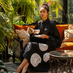 Woman in a black outfit with white patterns sitting on an orange couch holding a cup and saucer.