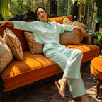 Woman in light green outfit sitting on an orange couch with plants in the background