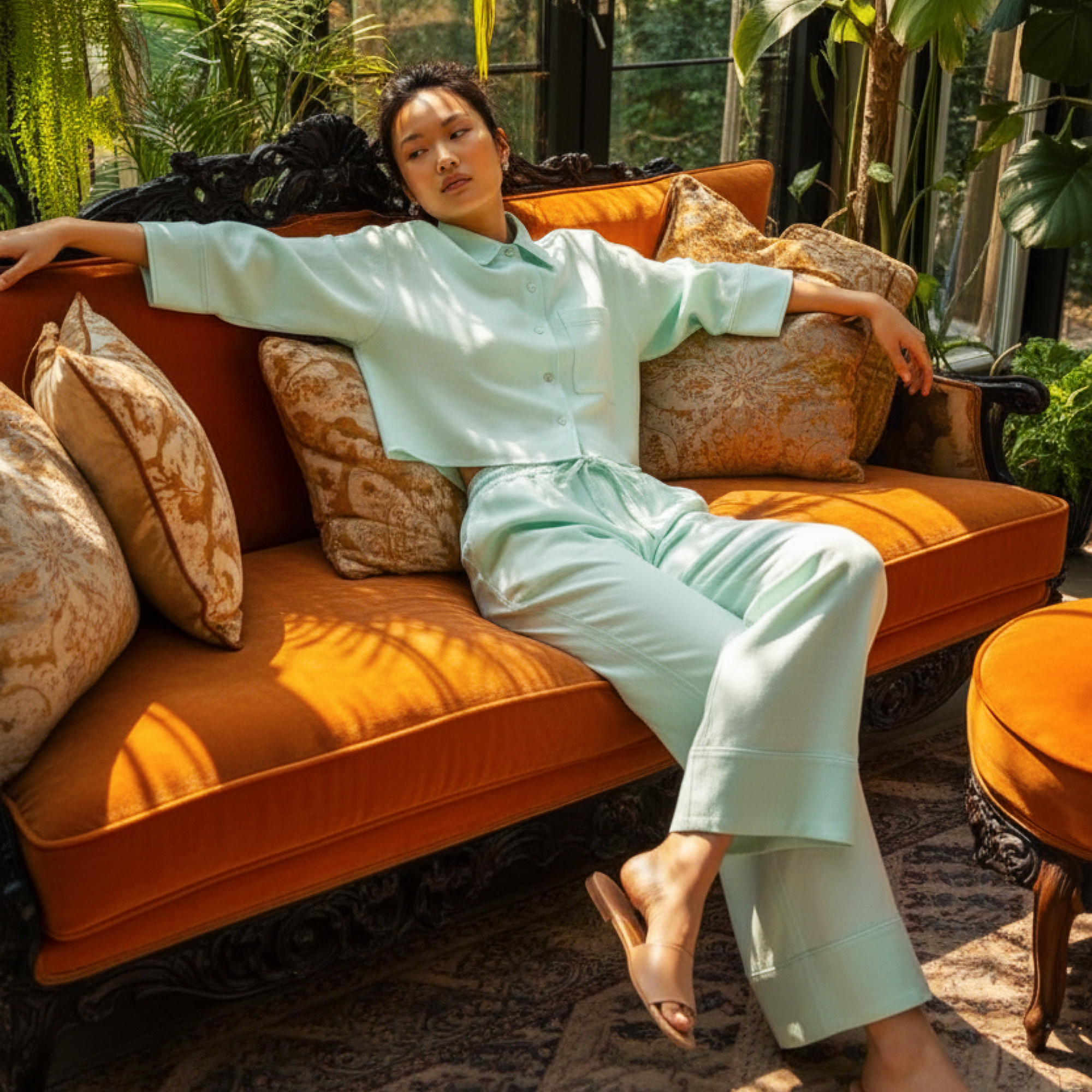Woman in light green outfit sitting on an orange couch with plants in the background
