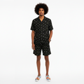 Man wearing a black patterned shirt and shorts set on a white background