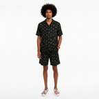 Man wearing a black patterned shirt and shorts set on a white background