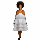 Young girl wearing a white tiered dress with a brown top on a black background