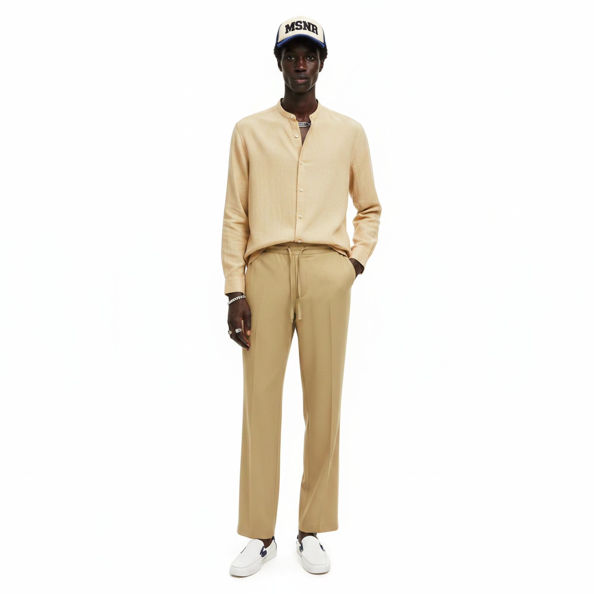 Man wearing a beige outfit with a cap on a white background