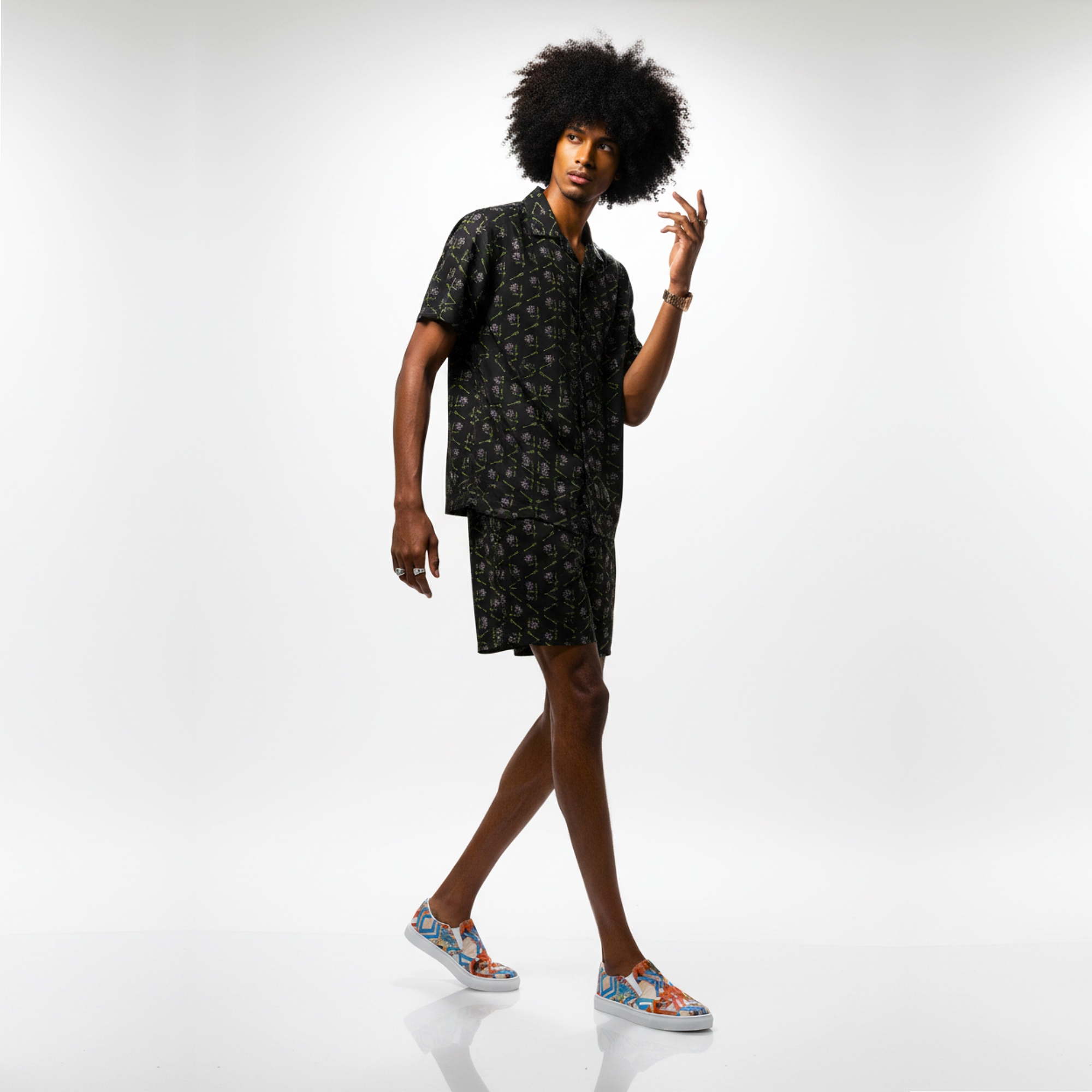 Person wearing a black patterned dress with colorful shoes on a white background