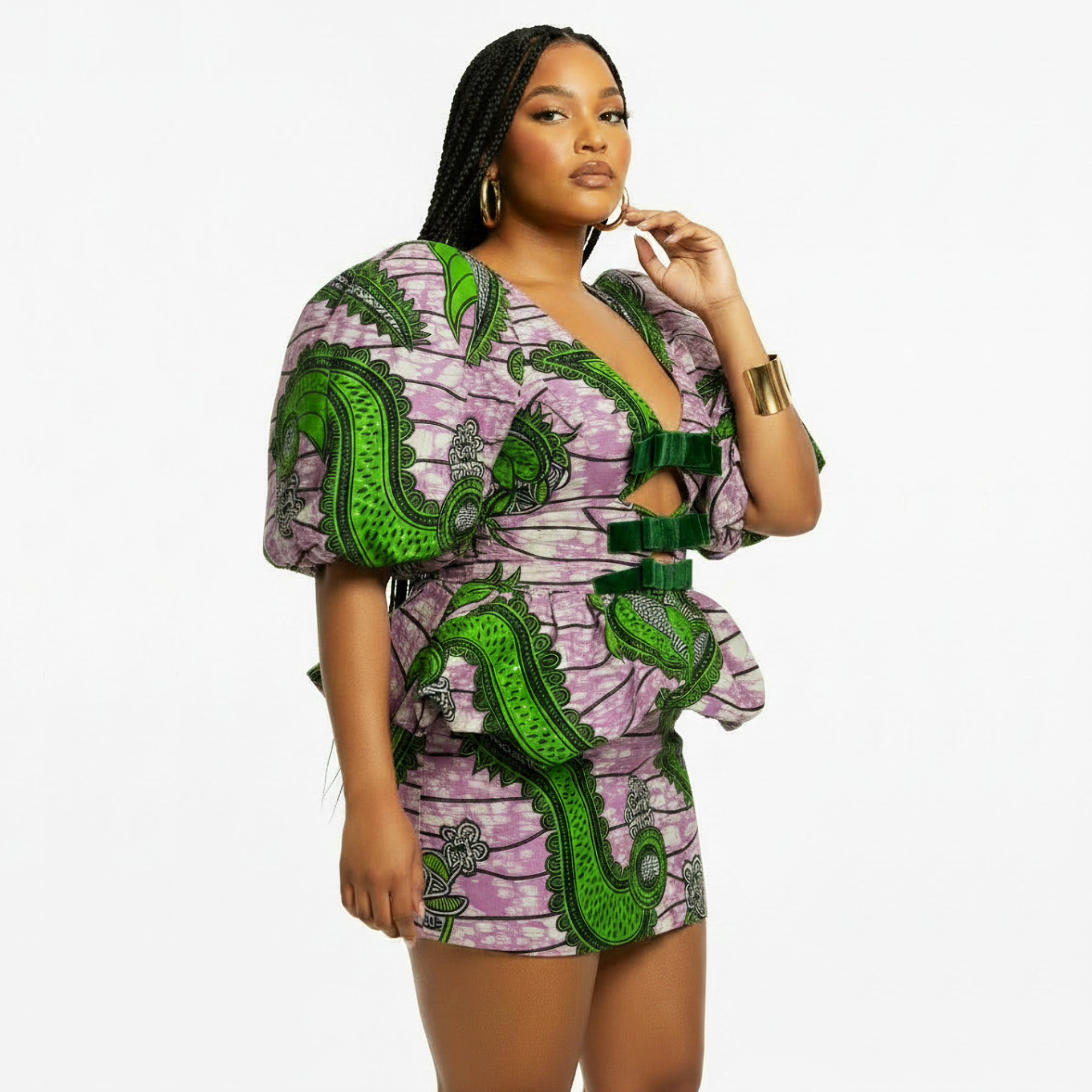 A woman modeling a short, puff-sleeve dress with a green and pink abstract print, featuring a deep V-neckline, side cutouts, and matching green belt details, set against a plain white background.