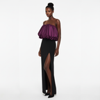 Woman wearing a strapless purple top and black high-slit skirt on a white background