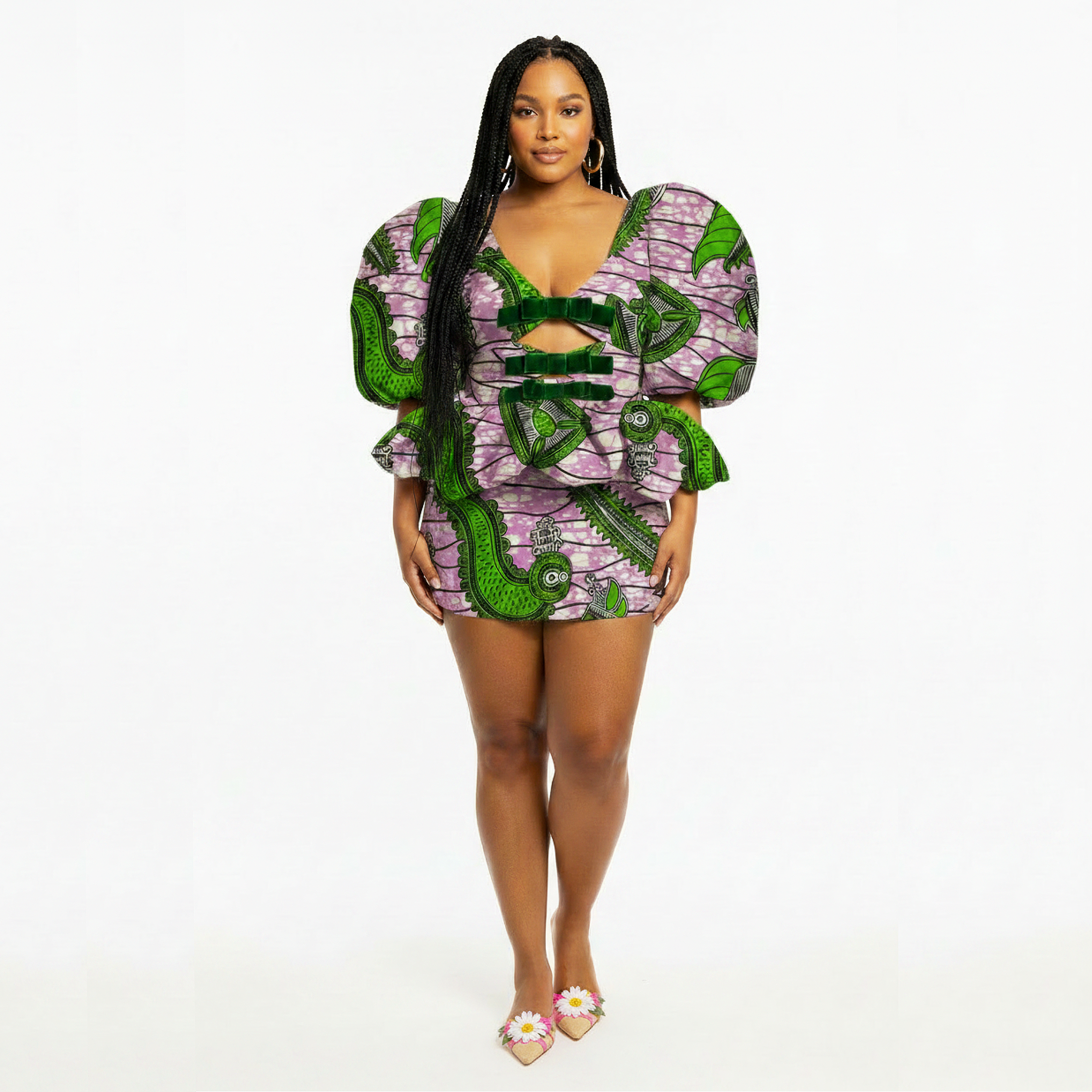 A woman modeling a matching two-piece outfit featuring a purple and green patterned short-sleeve top with puff sleeves and a matching mini skirt, set against a plain white studio background.