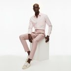 Man wearing a light pink shirt and pants sitting on a white stool against a white background