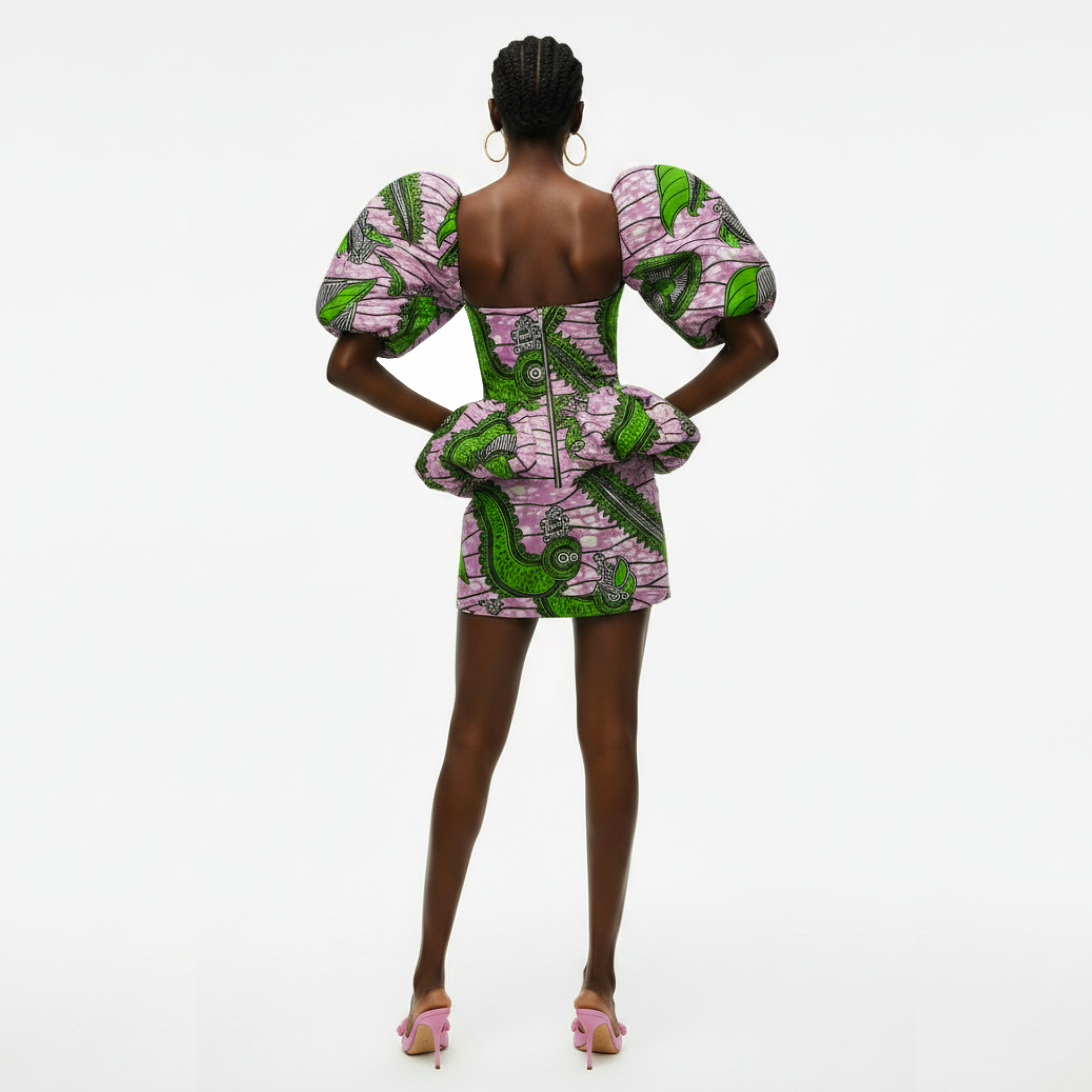 A model is shown from the back wearing a short puff-sleeve dress with a vibrant green and pink pattern, paired with pink high heels, against a plain white studio background.