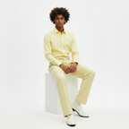 Man wearing a light yellow outfit sitting on a white cube against a white background