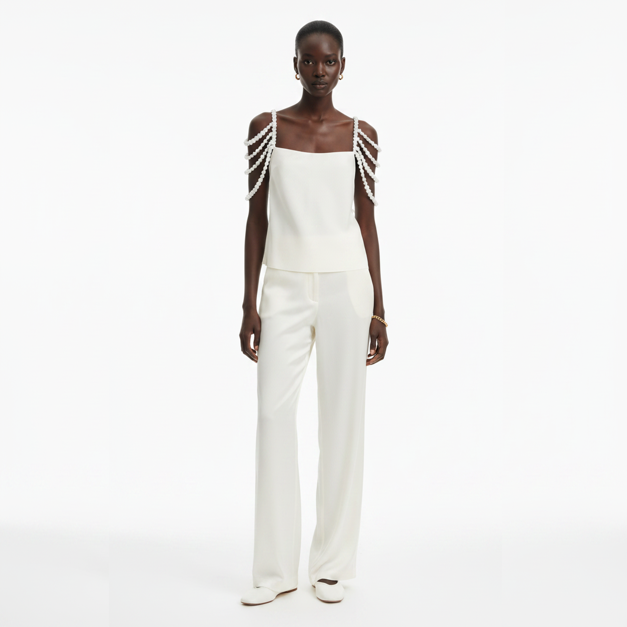 A person wearing a white top with pearl shoulder straps on a white background