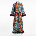 A long-sleeve, high-neck two-piece outfit with a bold orange, light blue, and black floral print, finished with black feather trim at the cuffs and hem, shown against a plain white background.