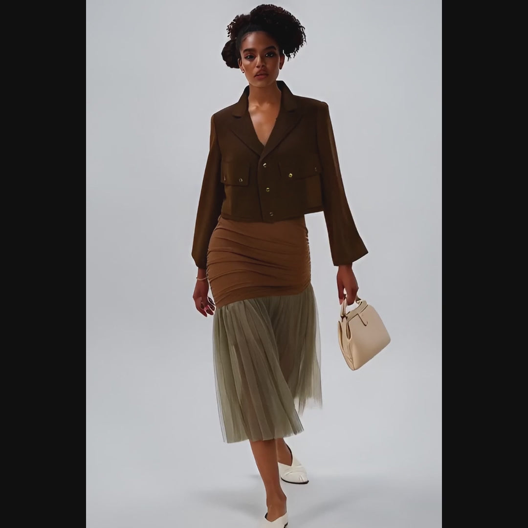 Woman wearing a brown jacket and skirt with a beige tulle hem on a white background
