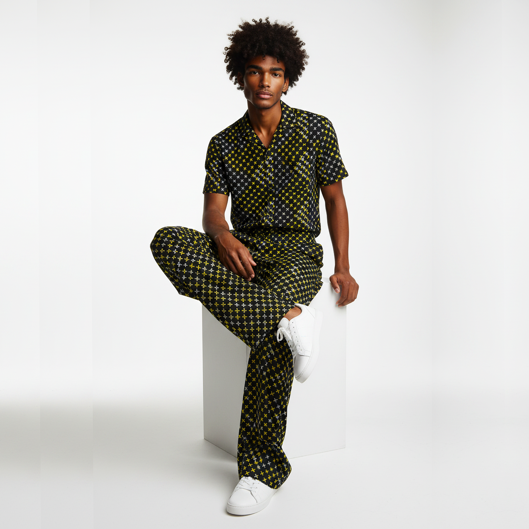 Man wearing a patterned outfit sitting on a white cube against a white background