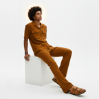 Man wearing a brown outfit sitting on a white cube against a white background