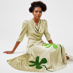 Woman wearing a beige dress with green clover patterns on a white background