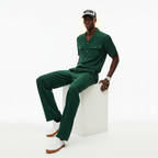 Man wearing a green outfit with a cap, sitting on a white cube against a white background