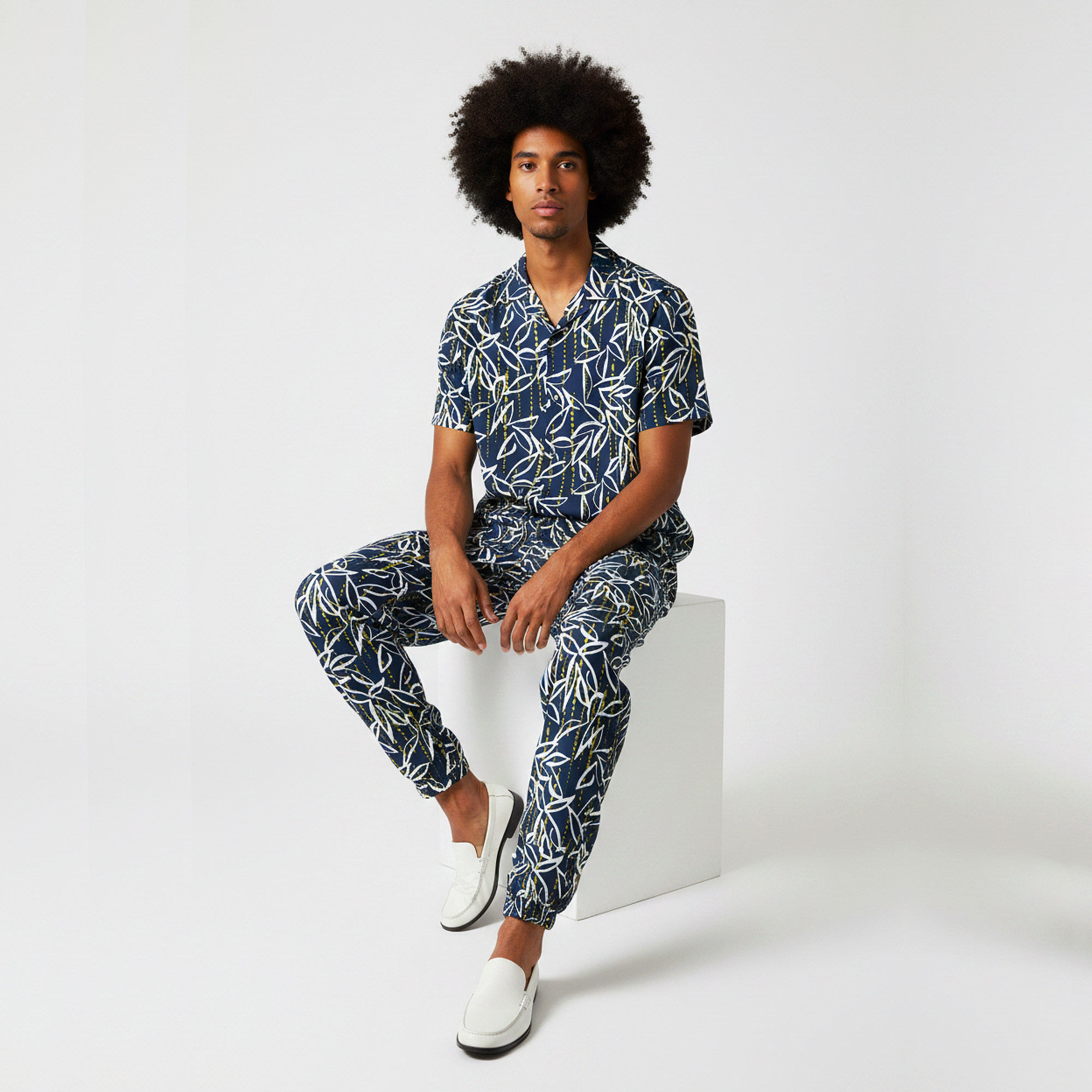 Man wearing a matching navy and white patterned shirt and pants sitting on a white block.