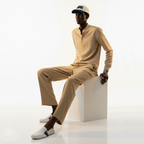 Man wearing a beige outfit with a cap, sitting on a white block against a white background